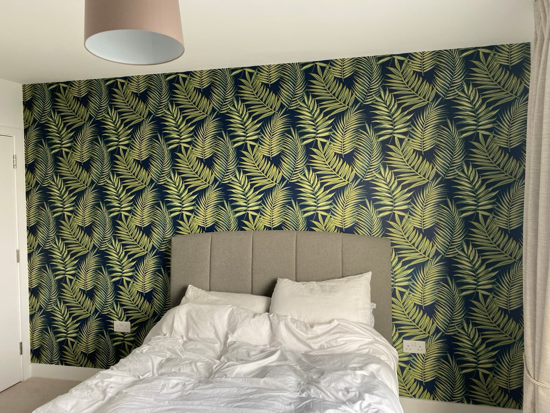 Bedroom feature wall in a green and navy palm leaf print behind an upholstered bed, the rest of the room left plain