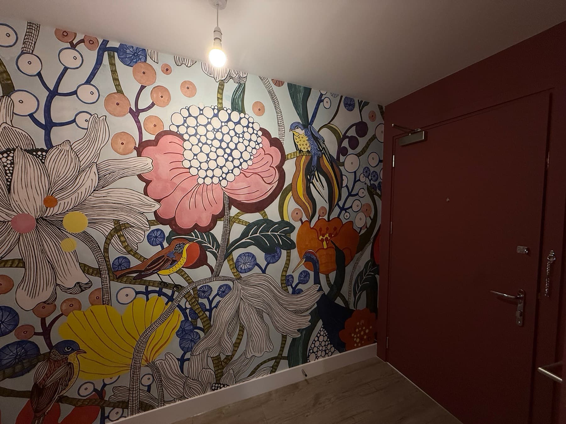 Oxblood painted door and lining cut in against a floral mural wallpaper and white skirting