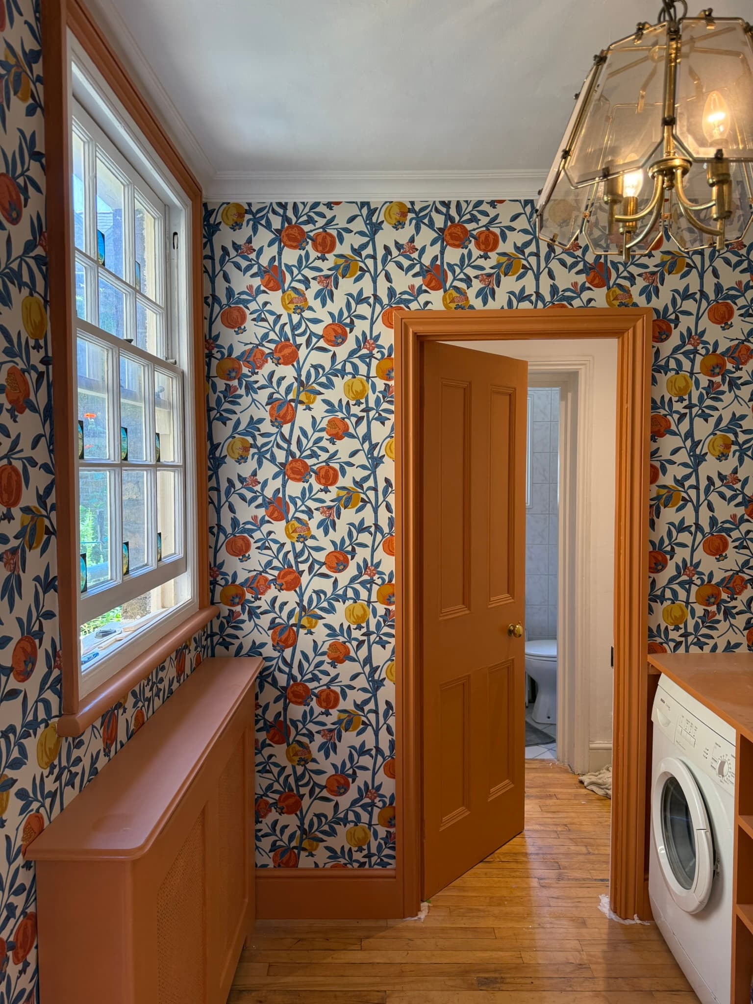 Hallway with pomegranate print floral wallpaper, terracotta painted woodwork, and a brass pendant light
